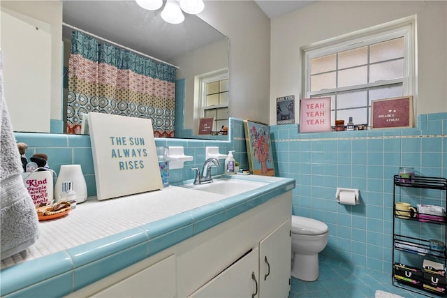 bathroom with tile patterned flooring, tile walls, a wainscoted wall, toilet, and vanity