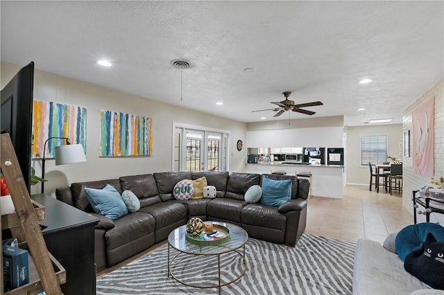 living area with light tile patterned floors, visible vents, a textured ceiling, and ceiling fan