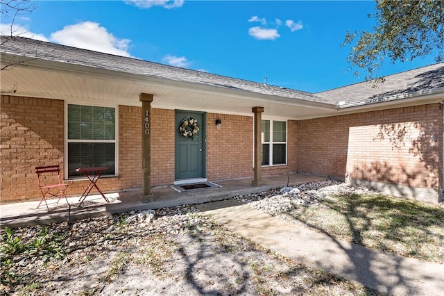 entrance to property featuring a porch and brick siding