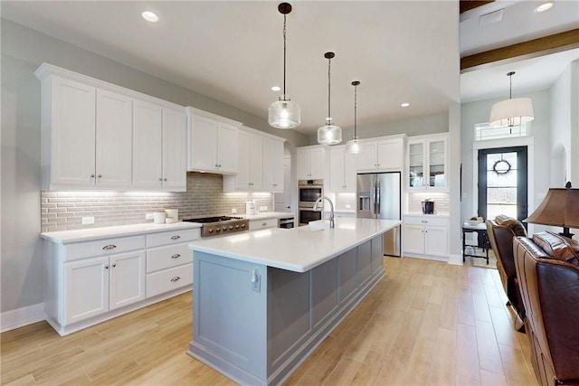 kitchen with white cabinets, light countertops, a center island with sink, glass insert cabinets, and pendant lighting