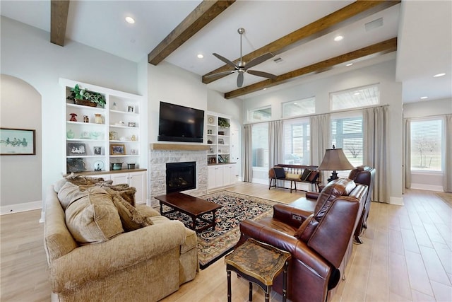 living room with a ceiling fan, a stone fireplace, light wood-style flooring, and baseboards