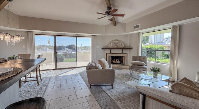 1406 Broken Hls Unit 14, Horseshoe Bay, TX 78657 - living area with stone tile floors, a fireplace with raised hearth, a chandelier, a ceiling fan, and beam ceiling