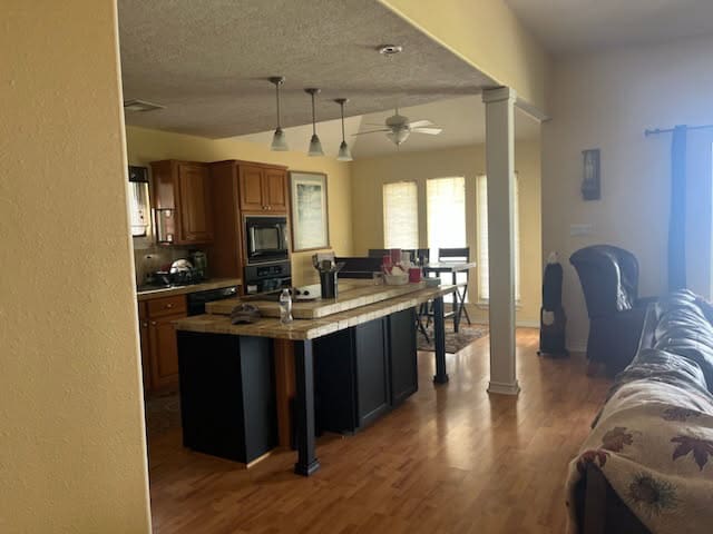231 Memphis Belle Ln, Trinity, TX 75862 - kitchen featuring black appliances, wood finished floors, brown cabinetry, ornate columns, and ceiling fan