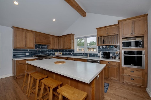 kitchen featuring a breakfast bar, backsplash, sink, light wood-type flooring, and appliances with stainless steel finishes