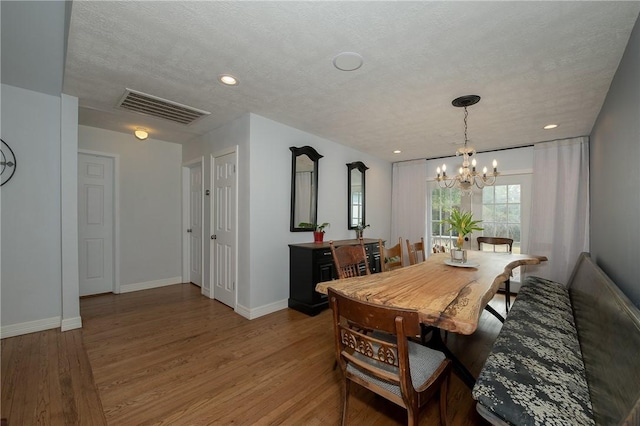 dining space with hardwood / wood-style flooring, a notable chandelier, and a textured ceiling