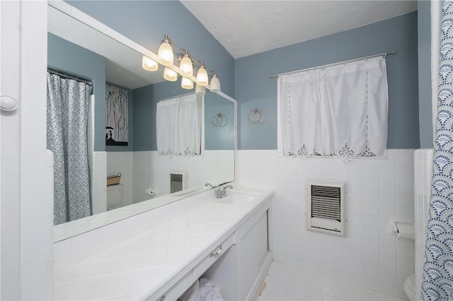 bathroom with vanity, heating unit, toilet, and tile walls