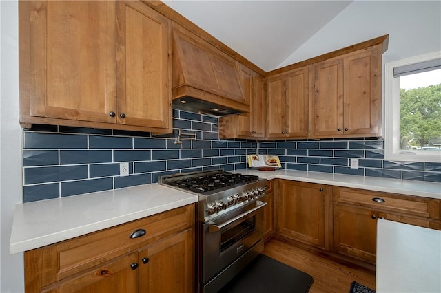 kitchen featuring decorative backsplash, custom range hood, vaulted ceiling, high end stainless steel range oven, and wood-type flooring