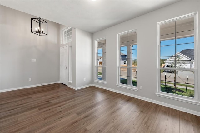 unfurnished room featuring an inviting chandelier, a wealth of natural light, and dark wood-type flooring