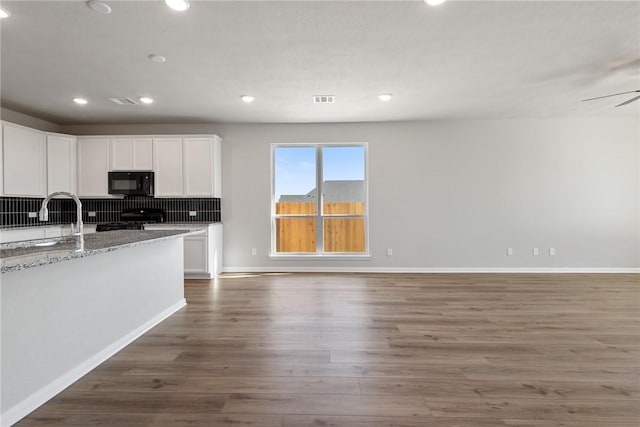 kitchen featuring stove, sink, dark hardwood / wood-style floors, light stone counters, and white cabinetry