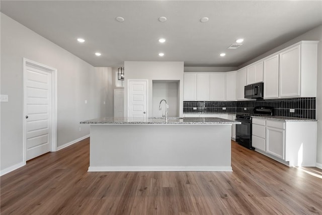 kitchen with an island with sink, white cabinets, black appliances, and light hardwood / wood-style floors