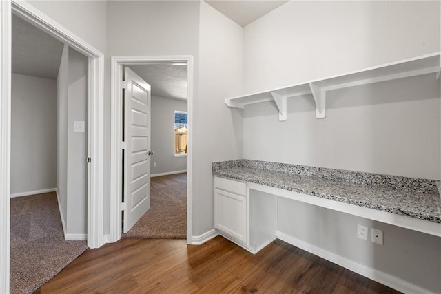 interior space with built in desk, white cabinetry, dark wood-type flooring, and light stone counters