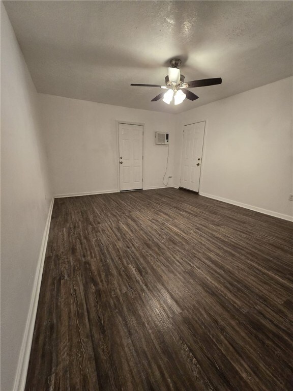 unfurnished bedroom featuring a textured ceiling, a wall mounted AC, ceiling fan, and dark hardwood / wood-style floors