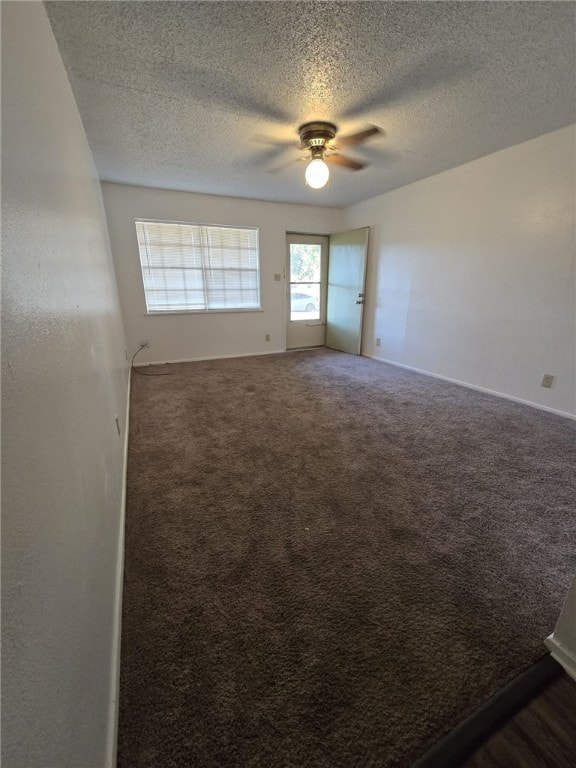 spare room featuring ceiling fan, dark carpet, and a textured ceiling