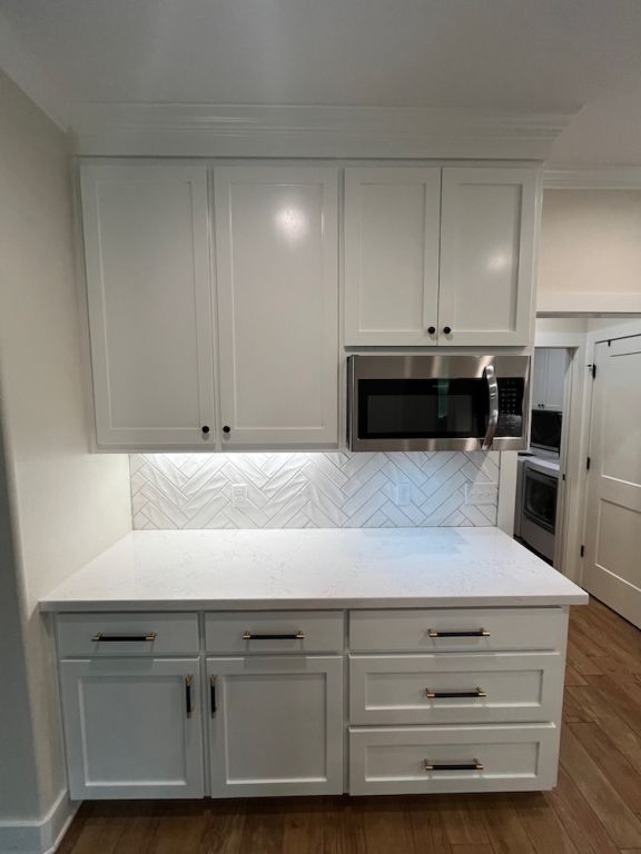 2016 R A Galindo Blvd, Bryan, TX 77807 - kitchen featuring stainless steel microwave, decorative backsplash, dark wood-style flooring, white cabinets, and ornamental molding