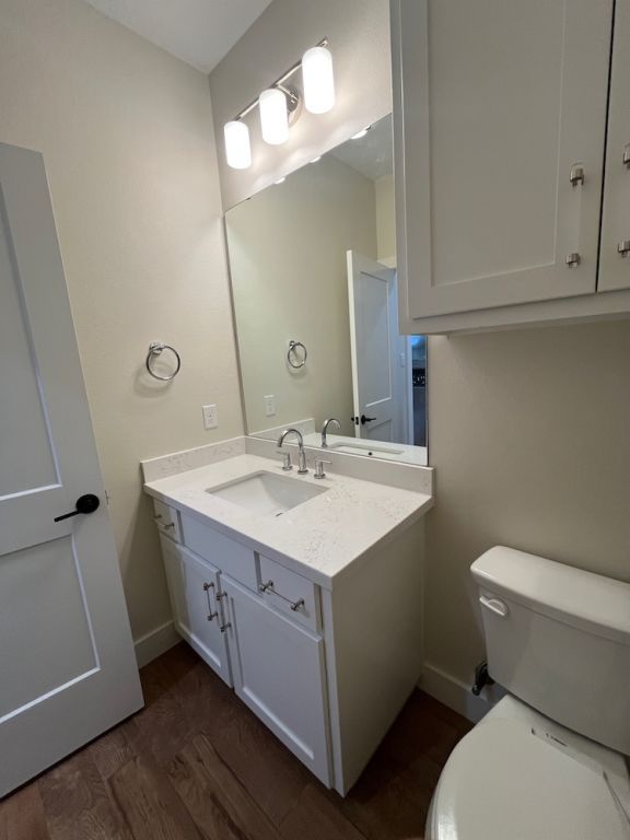2016 R A Galindo Blvd, Bryan, TX 77807 - half bathroom featuring vanity, toilet, baseboards, and wood finished floors