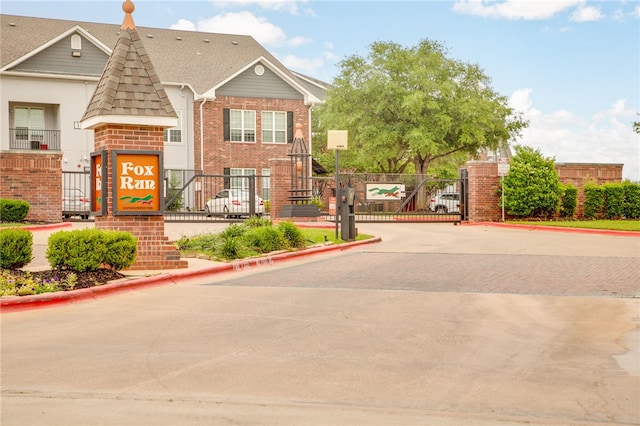 exterior space with fence, decorative driveway, brick siding, a gate, and a shingled roof