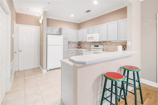 kitchen with decorative backsplash, a kitchen breakfast bar, light countertops, a peninsula, and white appliances