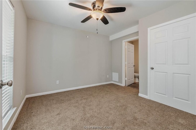 unfurnished bedroom featuring ceiling fan, carpet floors, multiple windows, and ensuite bath