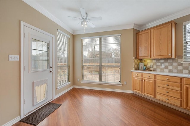 interior space featuring tasteful backsplash, baseboards, light countertops, crown molding, and light wood-type flooring