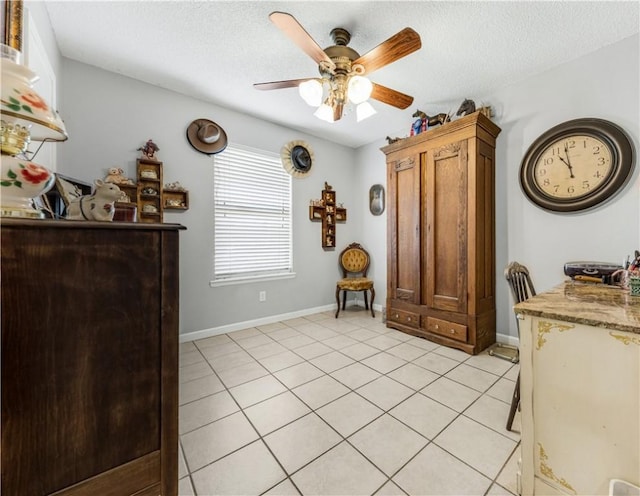 interior space with light tile patterned floors, baseboards, a textured ceiling, and ceiling fan