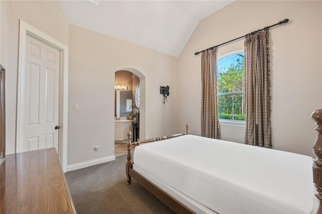 bedroom featuring dark colored carpet, ensuite bathroom, and lofted ceiling