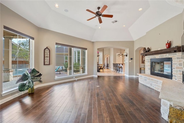 unfurnished living room featuring ceiling fan with notable chandelier, dark hardwood / wood-style flooring, a stone fireplace, and vaulted ceiling