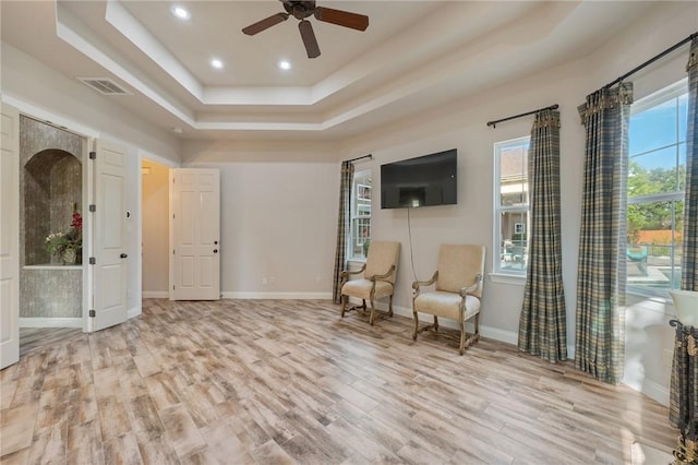 living area with ceiling fan, a raised ceiling, and light wood-type flooring