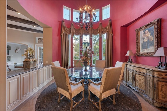 dining room with a notable chandelier, beam ceiling, and a towering ceiling