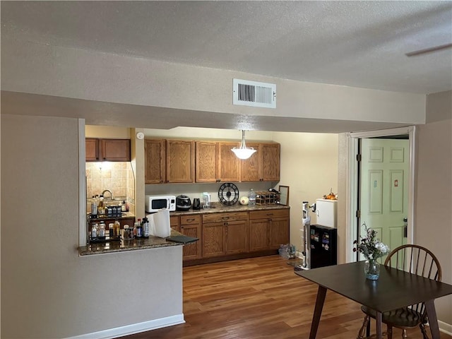 kitchen with decorative backsplash, wood-type flooring, a textured ceiling, and hanging light fixtures