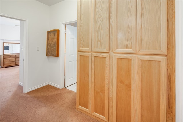 hallway featuring light colored carpet and baseboards