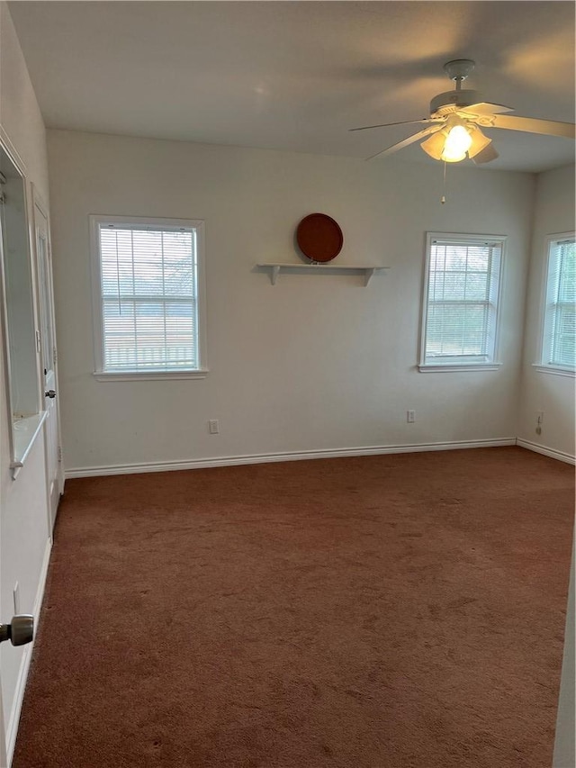 empty room with a ceiling fan, dark carpet, and baseboards