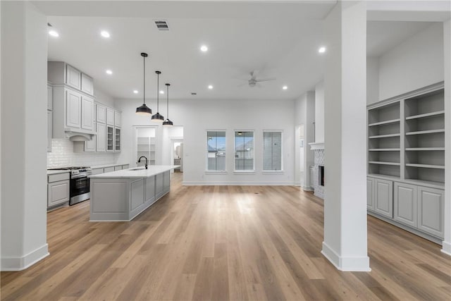 kitchen with decorative light fixtures, light hardwood / wood-style flooring, a kitchen island with sink, and stainless steel gas range oven