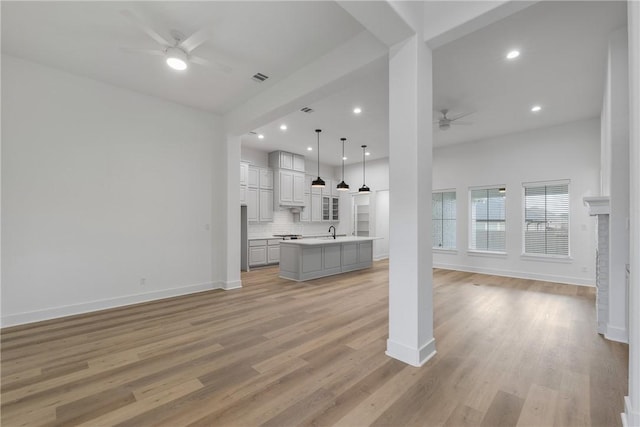 unfurnished living room featuring a fireplace, ceiling fan, sink, and light hardwood / wood-style floors