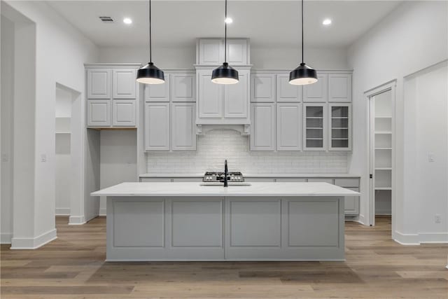 kitchen featuring sink, tasteful backsplash, pendant lighting, a kitchen island with sink, and light wood-type flooring