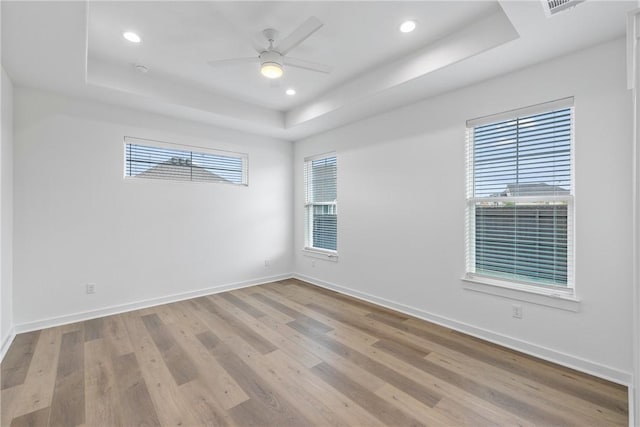 empty room with light hardwood / wood-style floors, a wealth of natural light, a tray ceiling, and ceiling fan