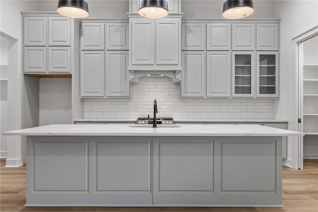 kitchen featuring light stone countertops, sink, an island with sink, and light hardwood / wood-style flooring