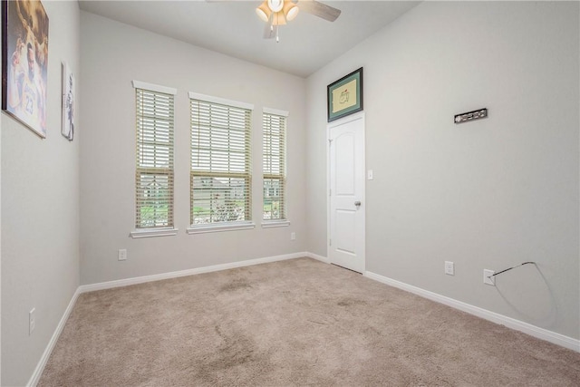 carpeted spare room featuring baseboards and a ceiling fan