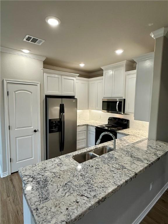 kitchen featuring appliances with stainless steel finishes, sink, white cabinets, kitchen peninsula, and light stone countertops