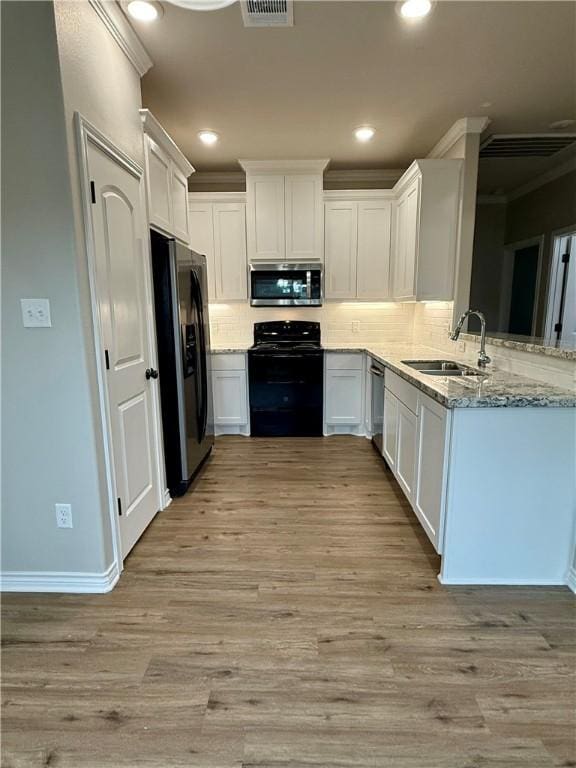 kitchen with sink, white cabinetry, light stone counters, light wood-type flooring, and appliances with stainless steel finishes