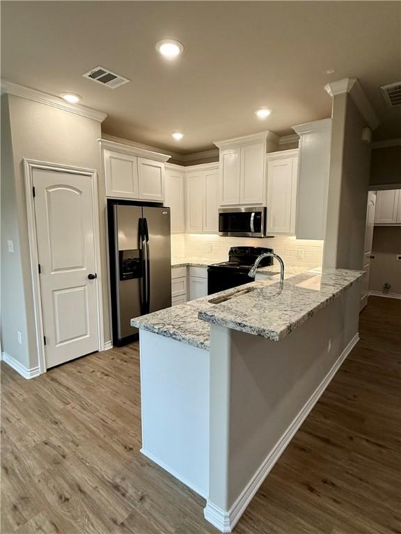 kitchen with white cabinetry, appliances with stainless steel finishes, kitchen peninsula, hardwood / wood-style flooring, and light stone countertops