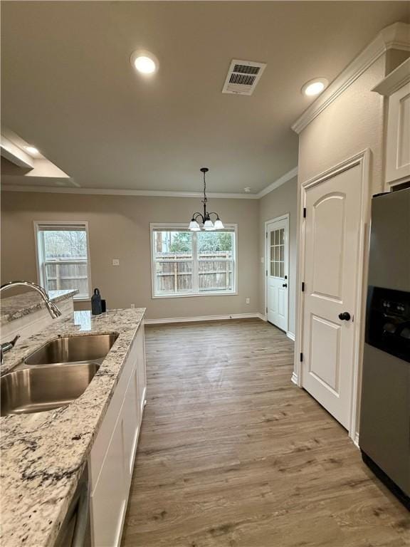 kitchen with white cabinetry, sink, decorative light fixtures, and stainless steel fridge