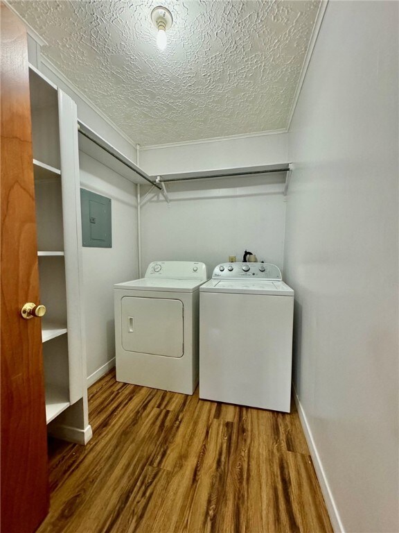 clothes washing area featuring independent washer and dryer, electric panel, wood-type flooring, a textured ceiling, and ornamental molding