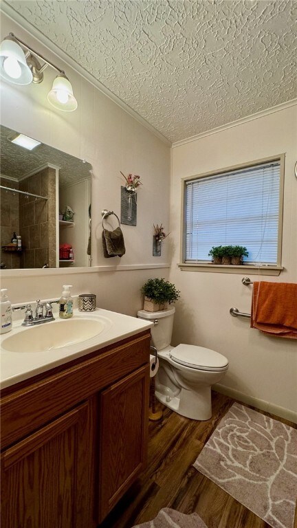 bathroom with a textured ceiling, vanity, tiled shower, wood-type flooring, and toilet