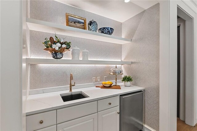 bar with a sink, fridge, indoor wet bar, backsplash, and stainless steel dishwasher
