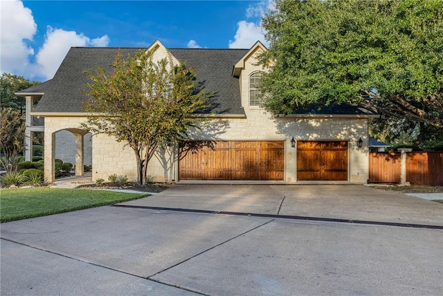 view of front of property with driveway, fence, a garage, stone siding, and roof with shingles
