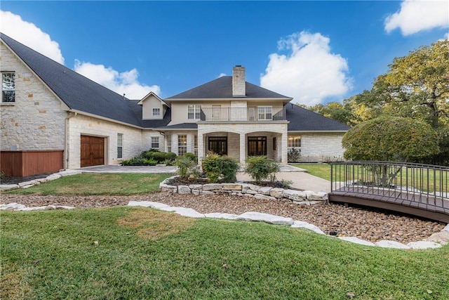 exterior space with stone siding, a balcony, concrete driveway, a front lawn, and a chimney