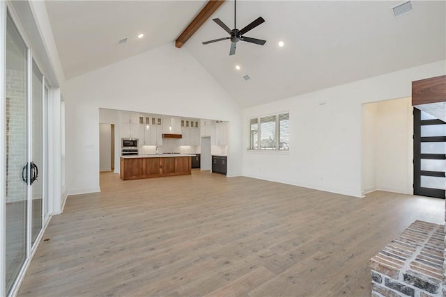 unfurnished living room featuring sink, ceiling fan, high vaulted ceiling, beamed ceiling, and light wood-type flooring