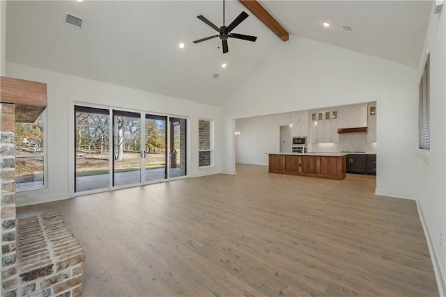 unfurnished living room featuring beam ceiling, hardwood / wood-style flooring, high vaulted ceiling, and ceiling fan