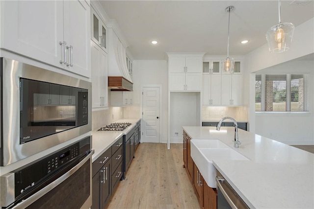 kitchen featuring appliances with stainless steel finishes, decorative light fixtures, white cabinetry, sink, and light hardwood / wood-style floors