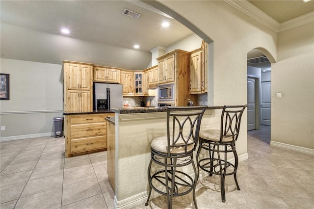 2703 Wood Ct, Bryan, TX 77808 - kitchen with appliances with stainless steel finishes, dark countertops, arched walkways, a peninsula, and light tile patterned flooring